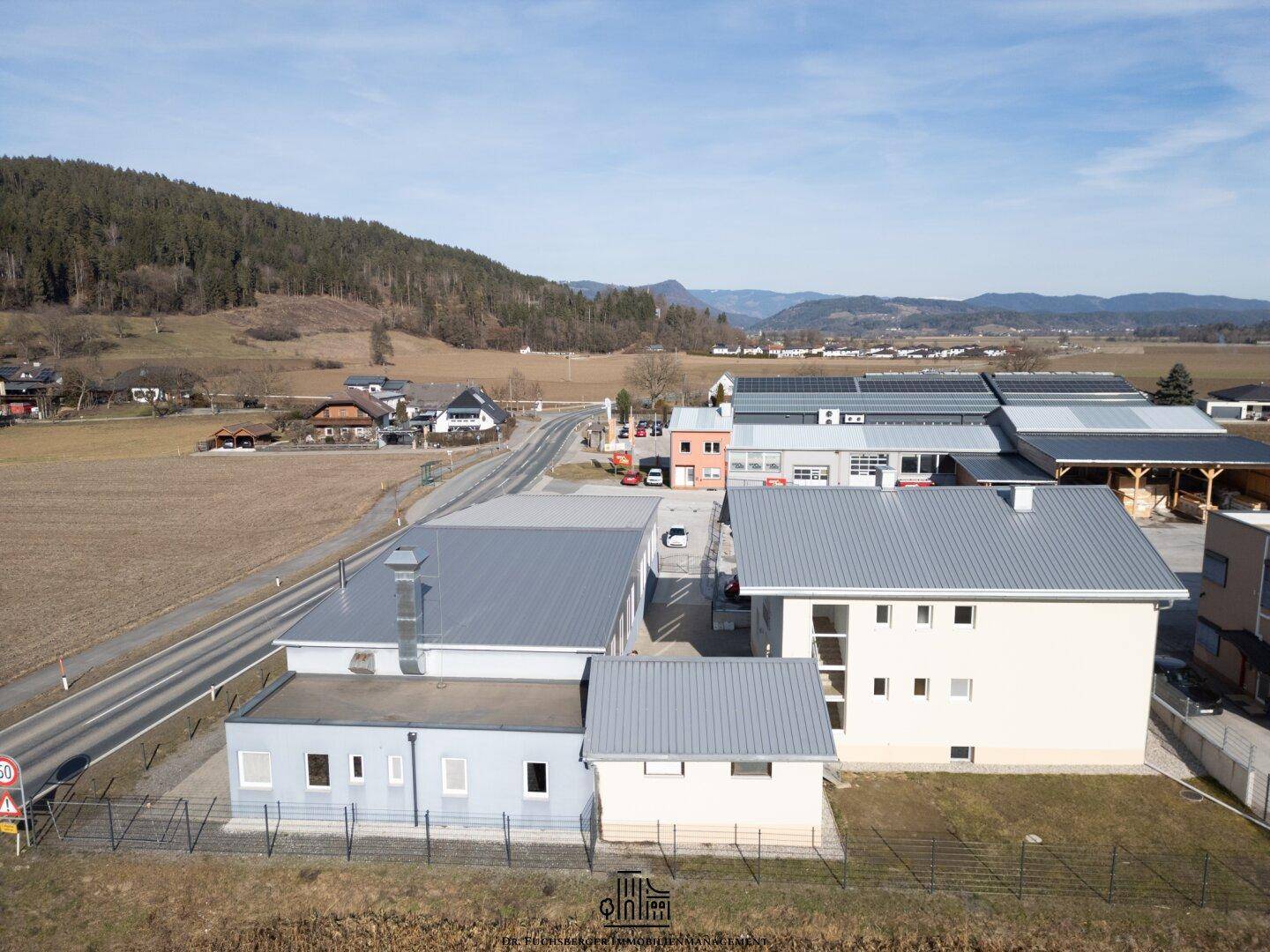 Luftaufnahme des Anwesens mit Wohnhaus, Gewerbegebäuden und Blick auf die bergige Umgebung.