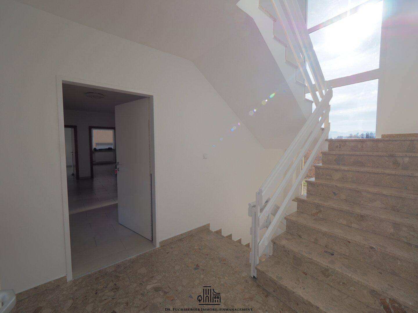 Heller Eingangsbereich mit Marmorboden und Treppe zum Obergeschoss, bietet einen eleganten Empfang.