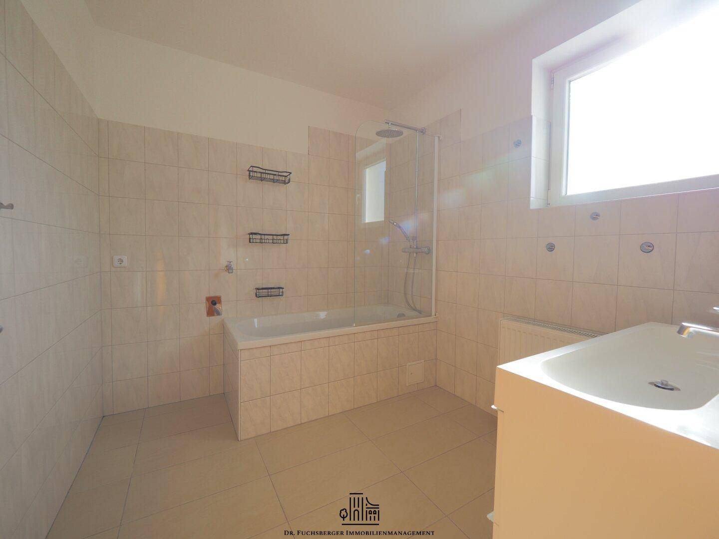 Helles Badezimmer mit Badewanne, Dusche und Waschtisch, ausgestattet mit modernen Fliesen und Fenster.