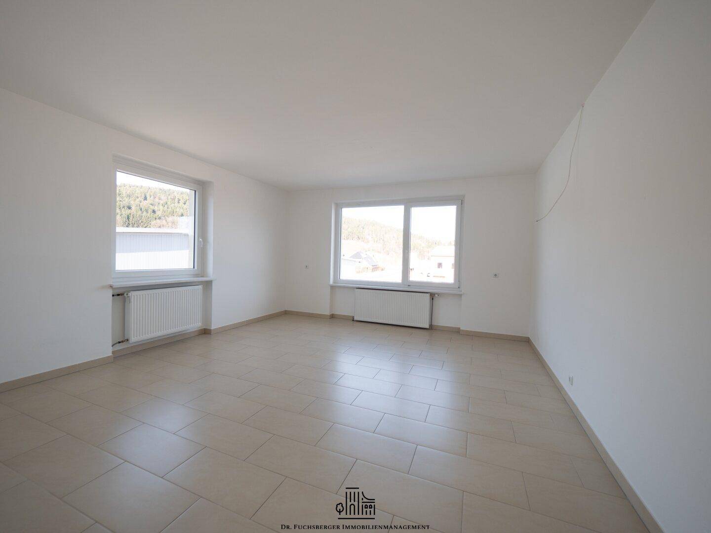 Großer, heller Raum mit Fliesenboden und zwei Fenstern, bietet viel Tageslicht und Platz.