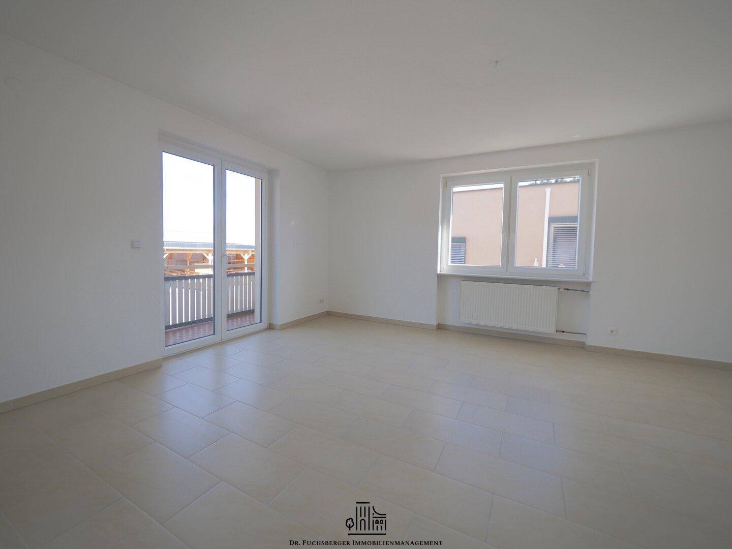 Lichtdurchfluteter Wohnraum mit Fliesenboden und breiter Balkontür, bietet viel Platz und Helligkeit.