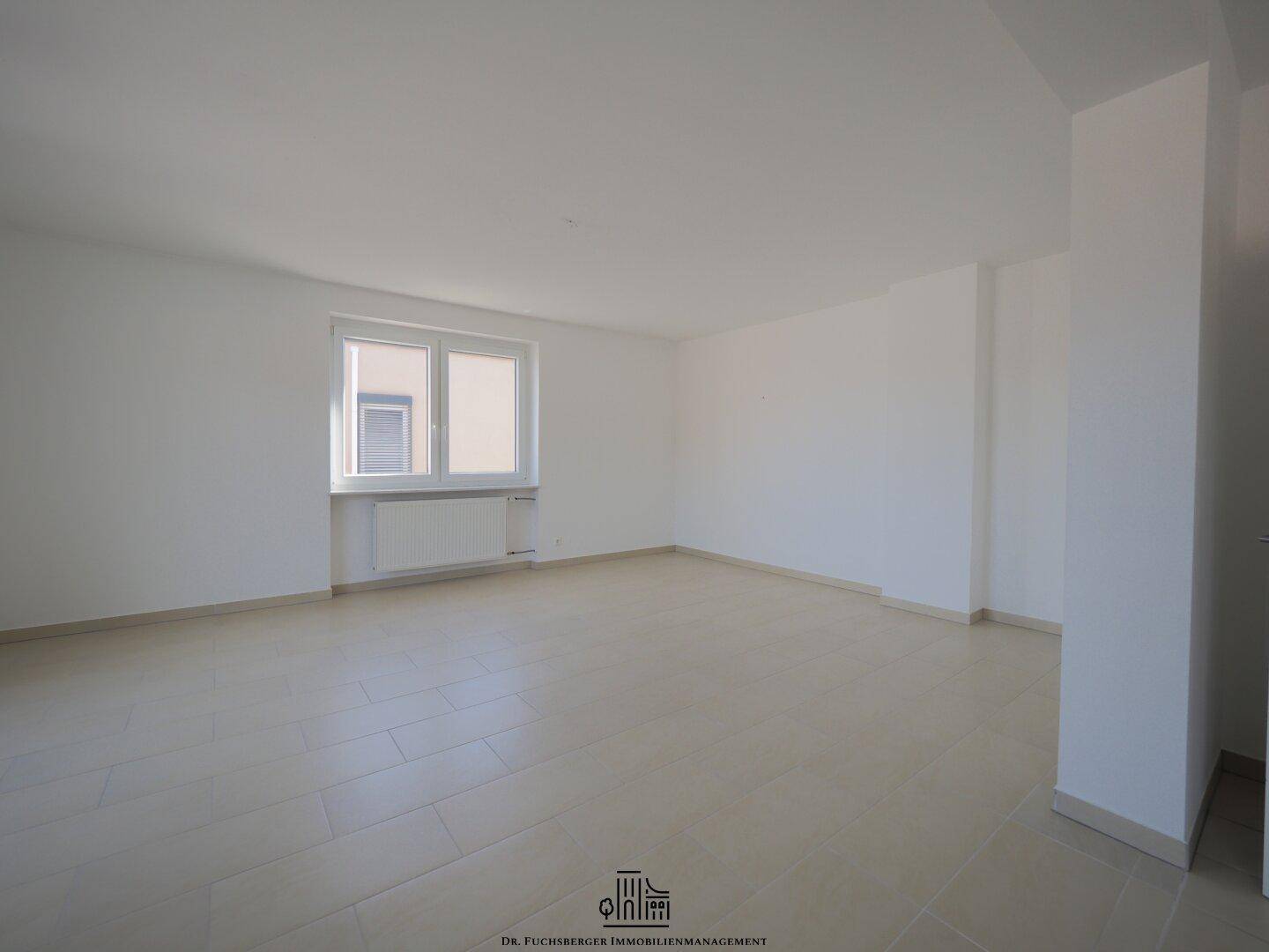 Geräumiger, heller Raum mit Fliesenboden und großem Fenster, ideal als Wohn- oder Schlafzimmer nutzbar.