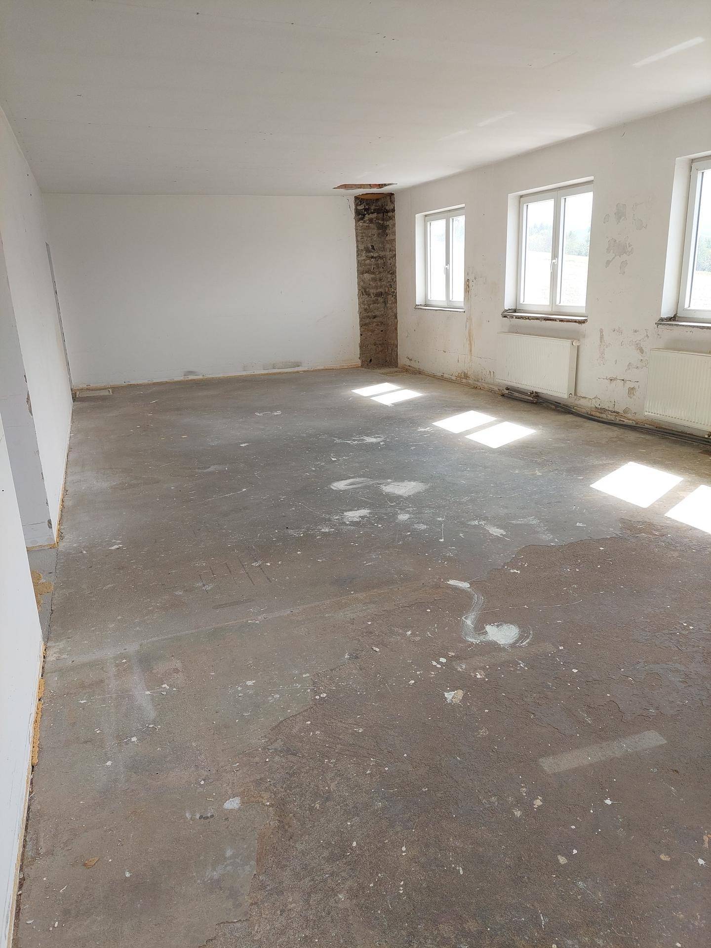 Heller, leerer Raum mit Betonboden, sichtbaren Heizkörpern und Spuren von Abnutzung an den Wänden.