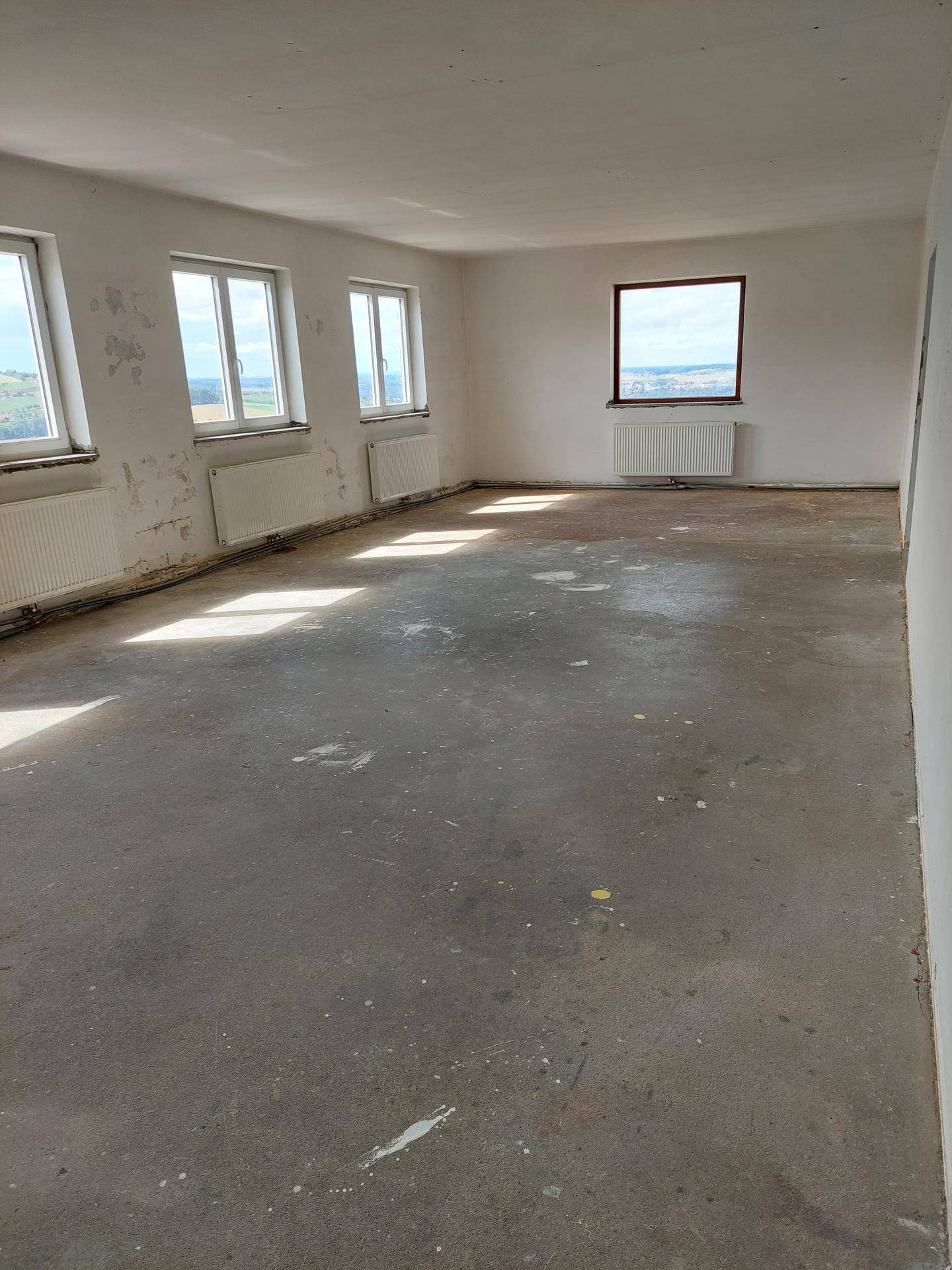 Geräumiger, heller Raum mit Betonboden, mehreren Fenstern und Heizkörpern, bietet weite Aussicht.
