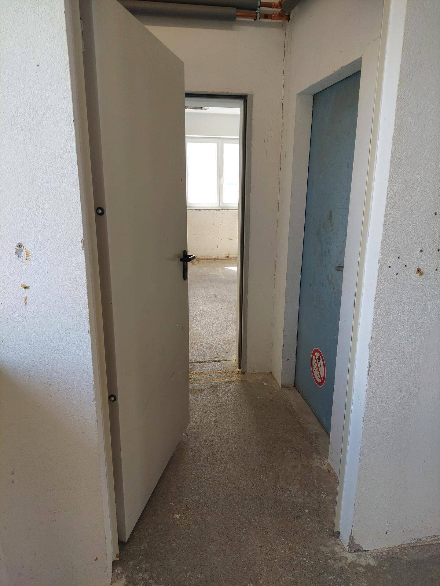 Schmaler Flur mit mehreren Türen, Betonboden und Blick in einen angrenzenden Raum.