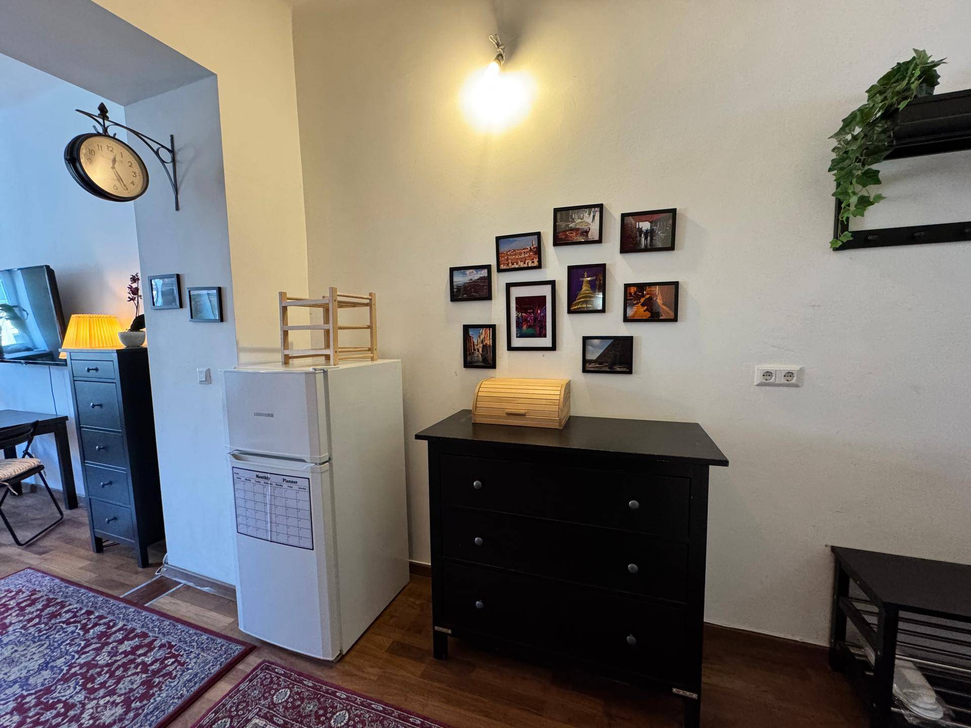 Flurbereich mit Kühlschrank, Kommode und dekorativen Bilderrahmen an der Wand.