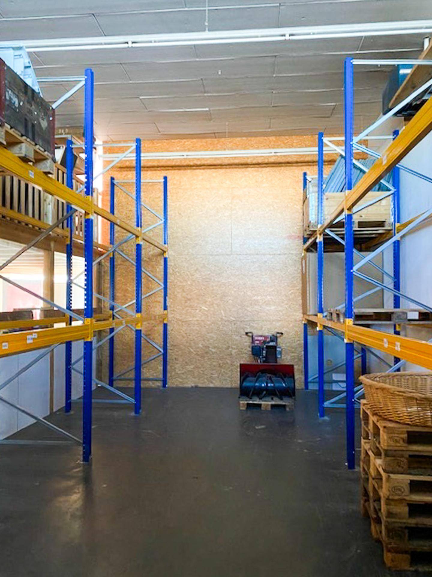 Lagerhalle mit hohen Regalen, Betonboden und einer Holzverkleidung an der Rückwand.