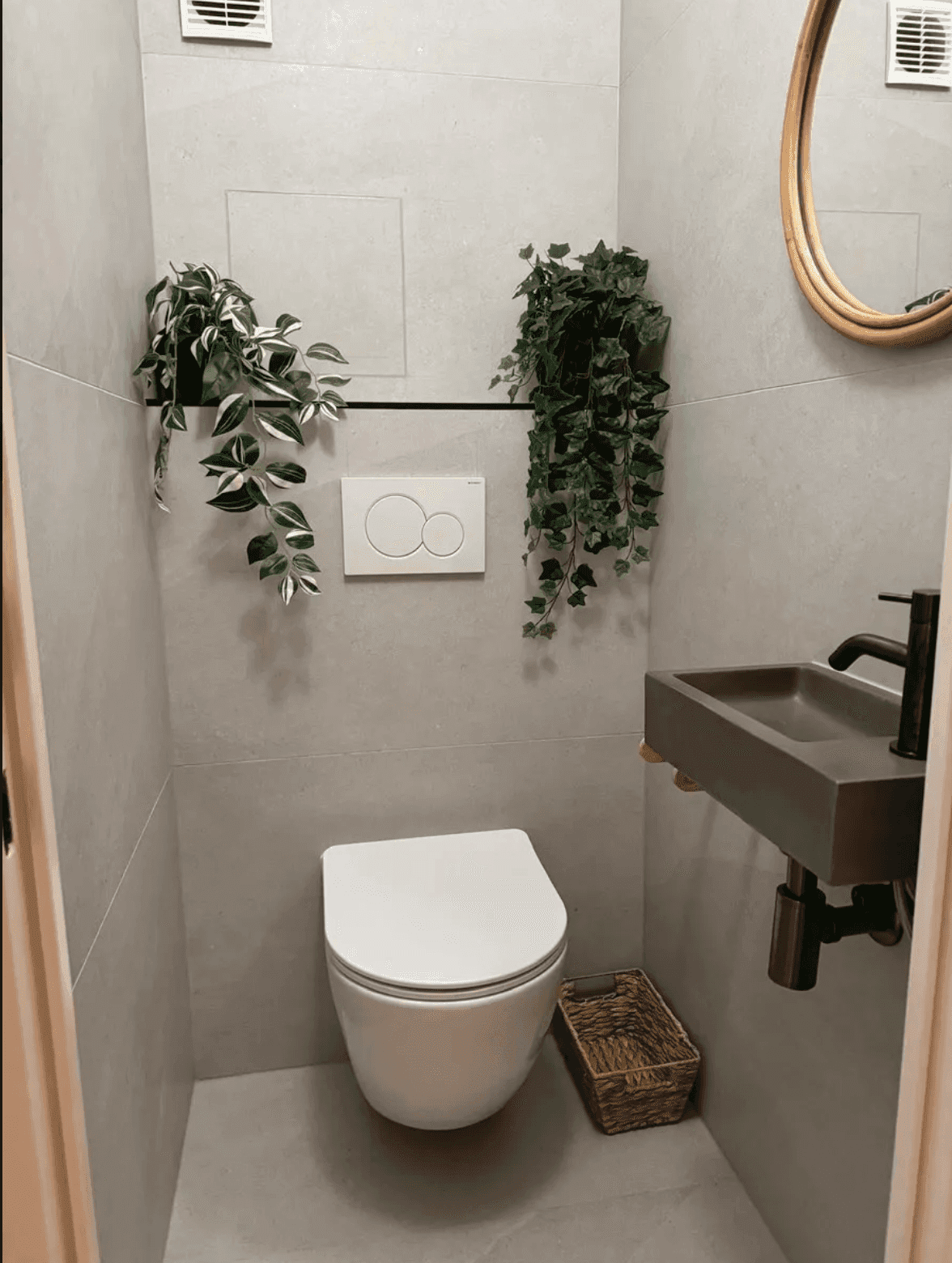 Modernes Gäste-WC mit grauen Fliesen, wandhängender Toilette und kleinem Waschbecken.