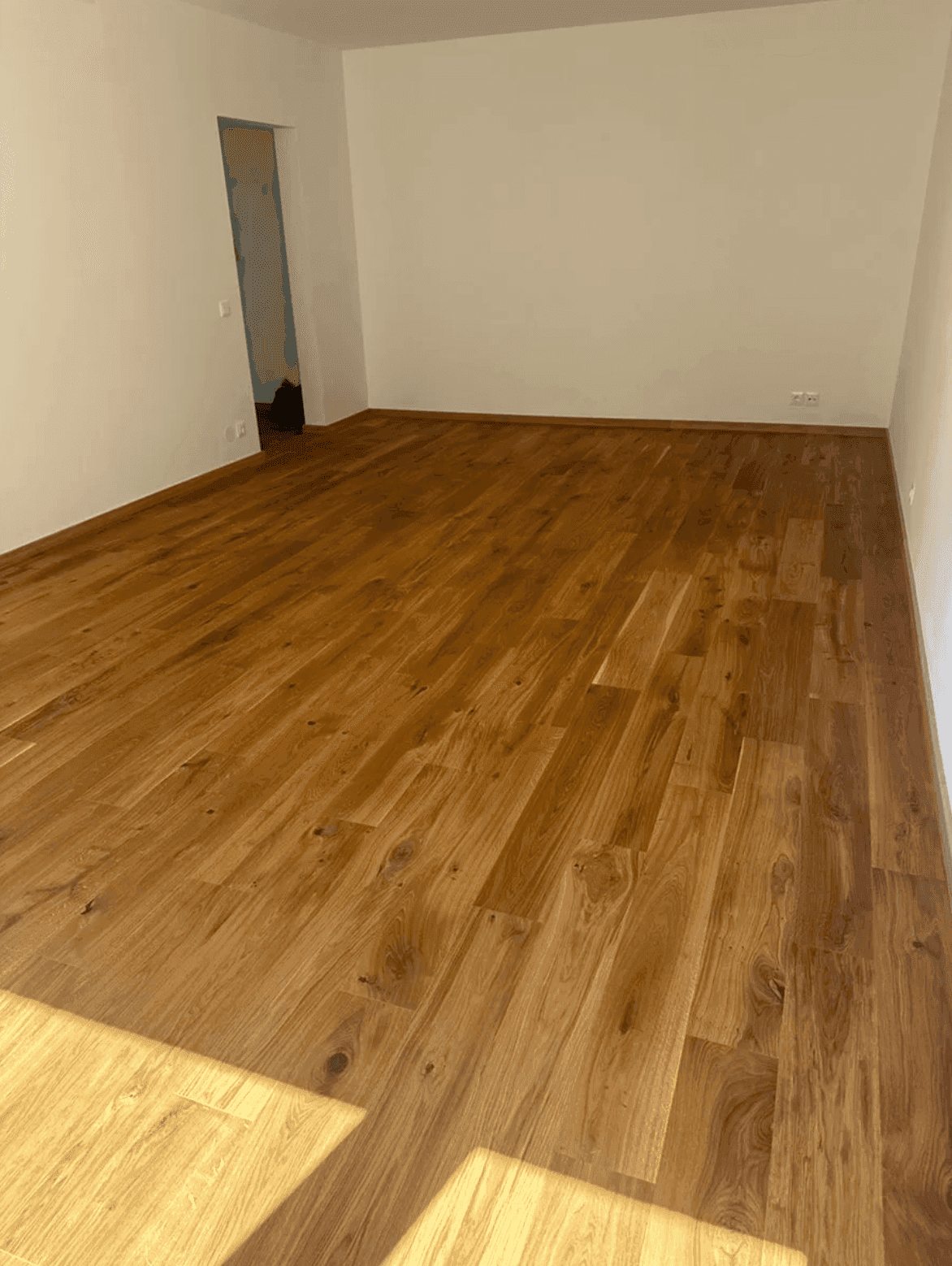 Geräumiges, leeres Zimmer mit hellem Holzfußboden und weißen Wänden, bereit zum Einrichten.