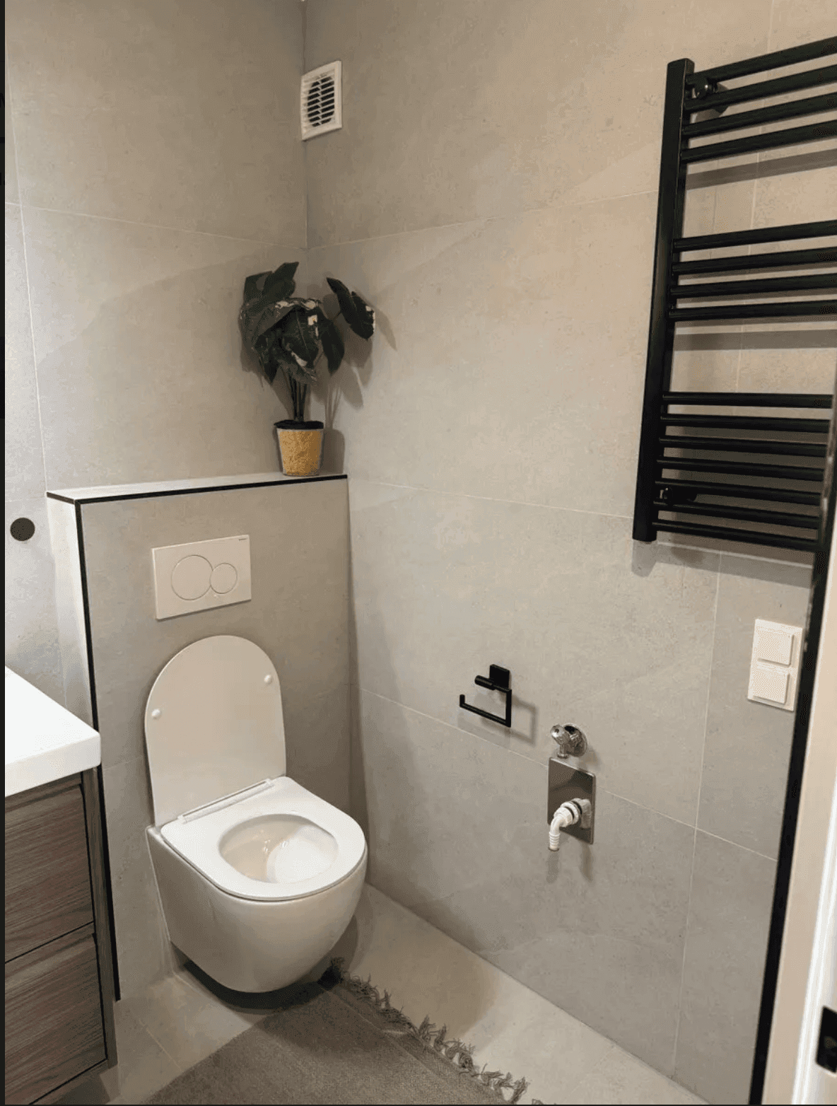 Helles Gäste-WC mit grauen Fliesen, wandhängender Toilette und beheiztem Handtuchhalter.