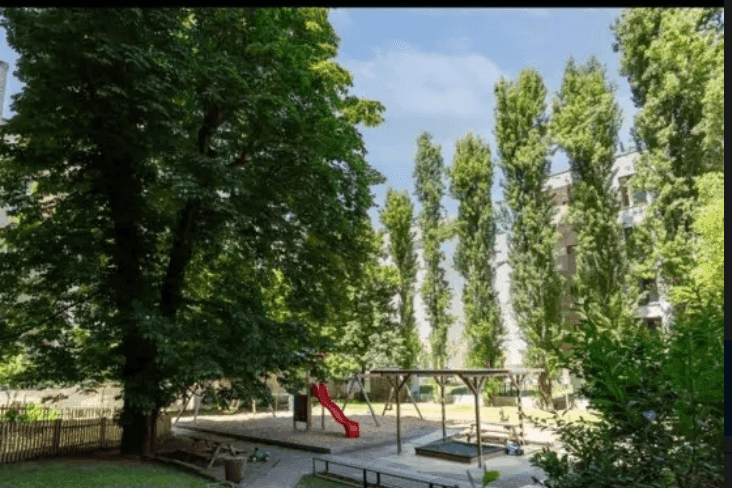 Weitläufiger Spielplatzbereich mit hohen Bäumen und viel Grün im Innenhof.