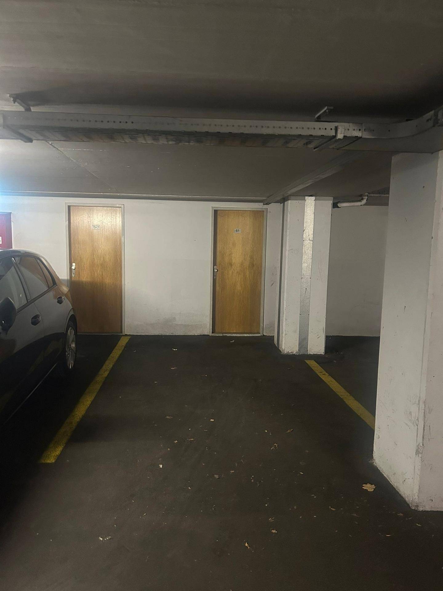 Tiefgarage mit markierten Parkplätzen und Zugang zu Kellerräumen.