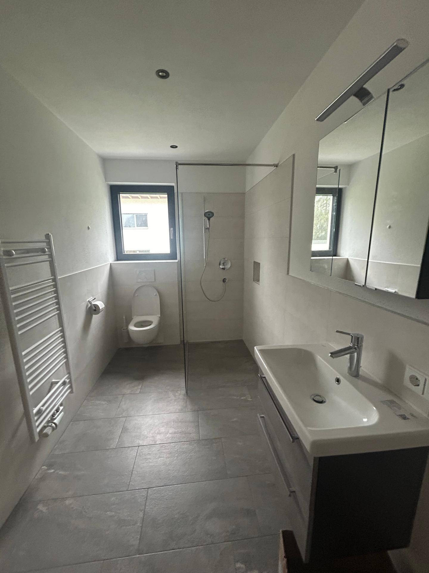 Modernes Badezimmer mit ebenerdiger Dusche, Hänge-WC, Einzelwaschbecken und Fenster für Tageslicht.