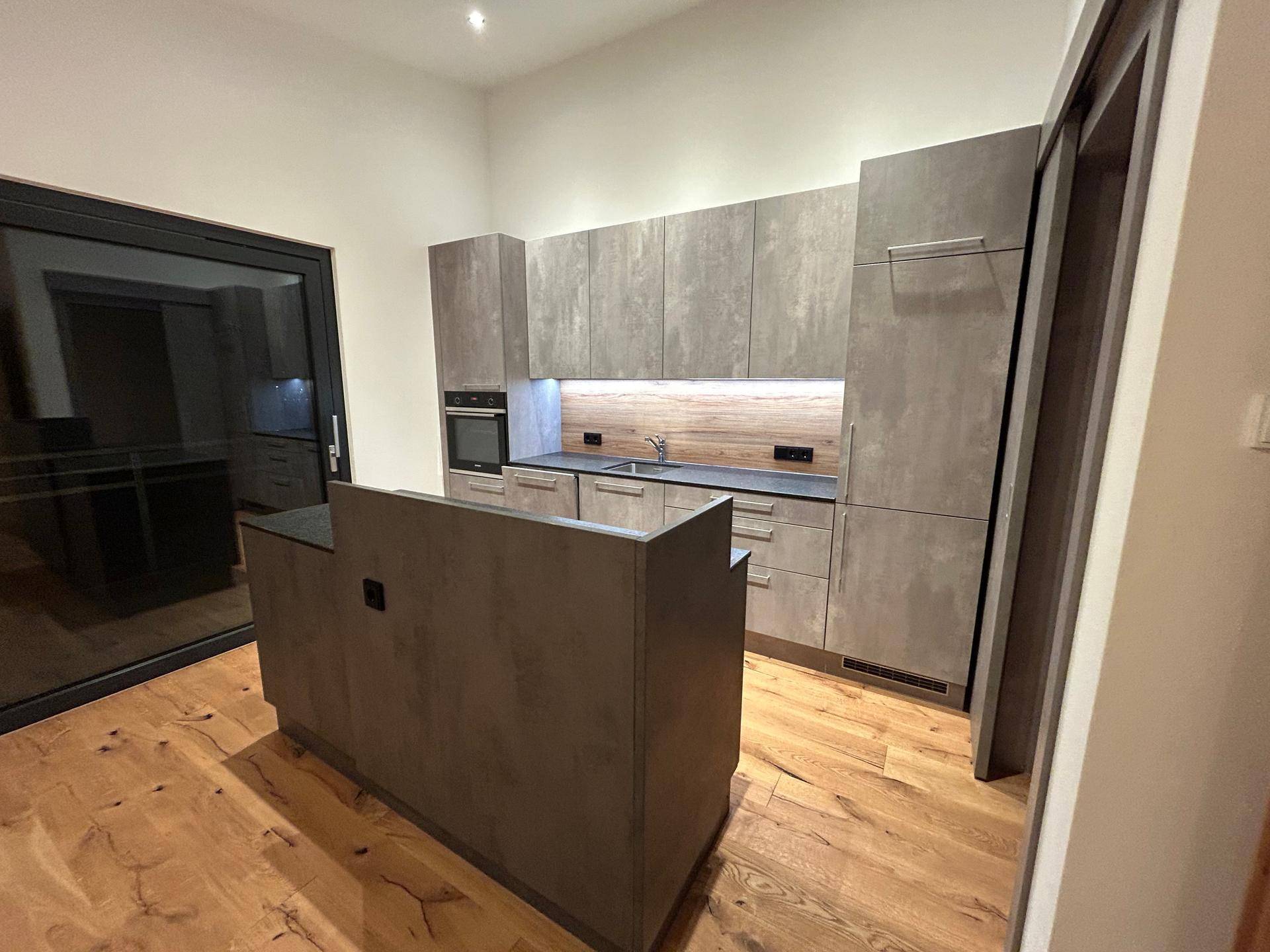 Moderne Einbauküche mit Kücheninsel, Holzfußboden und integrierten Geräten in neuwertigem Zustand.