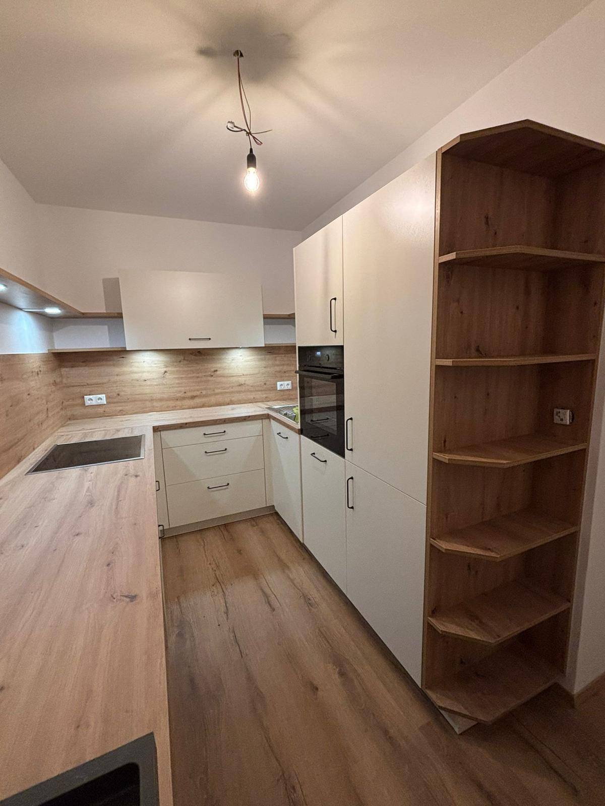 Moderne Einbauküche mit hellen Fronten, Holzarbeitsplatte und integriertem Backofen.