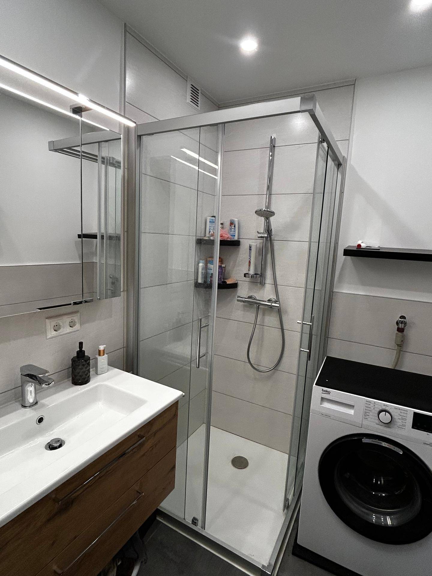 Modernes Badezimmer mit Duschkabine, Waschbecken und integrierter Waschmaschine.