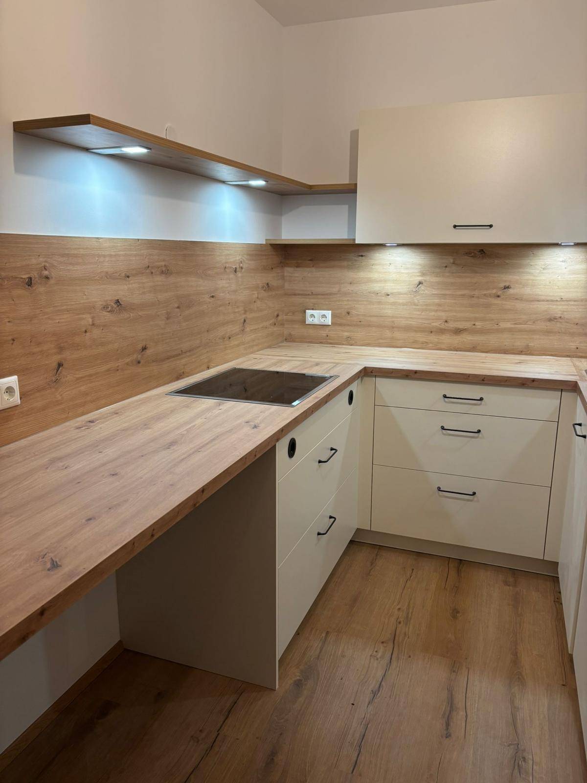 Helle Küche mit Holzdetails, integriertem Kochfeld und praktischen Regalen.