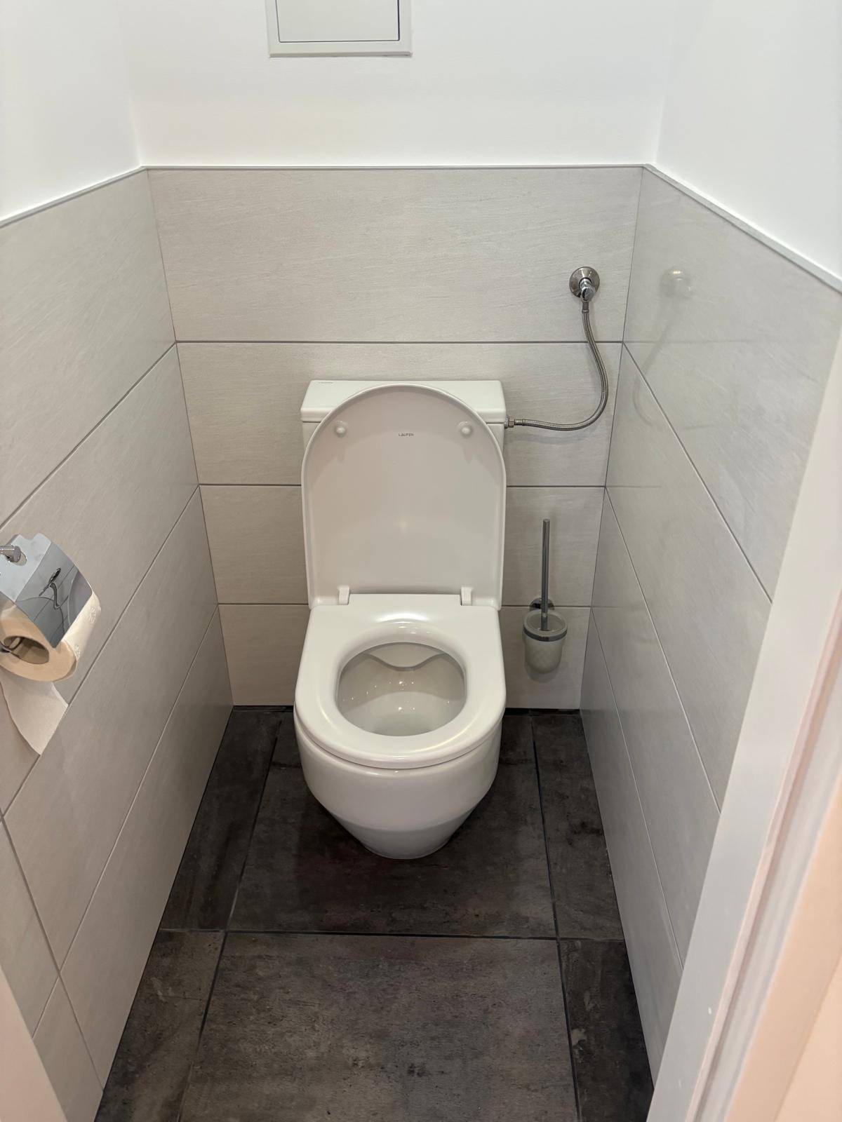 Separates WC mit modernen Fliesen und wandmontierter Toilette in hellem Design.