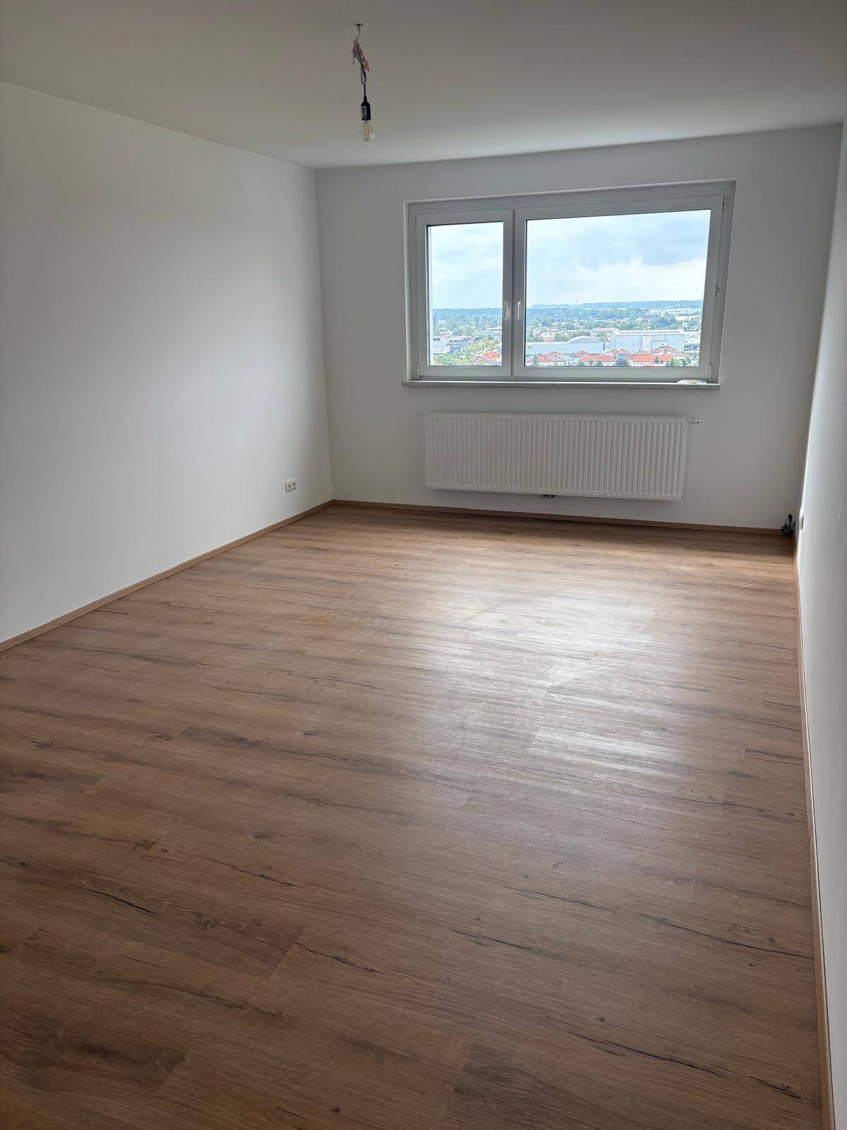 Geräumiges, helles Zimmer mit Laminatboden und großem Fenster mit Stadtblick.