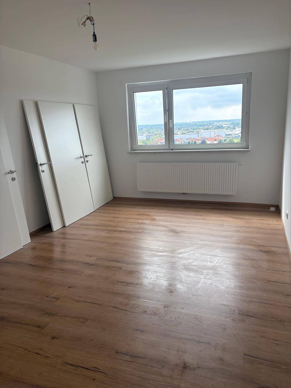Helles, leeres Zimmer mit Laminatboden und weitem Ausblick über die Stadt.