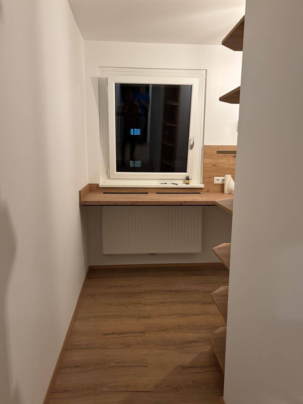 Kleiner, heller Raum mit Fenster, Heizung und praktischer Holzablagefläche.