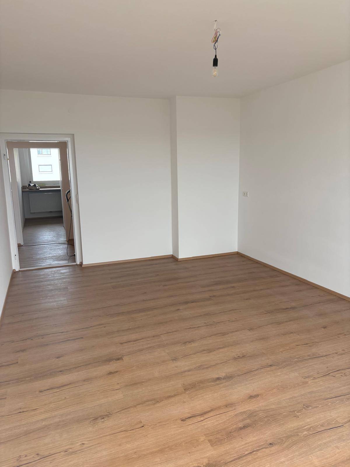 Heller Wohnbereich mit Laminatboden und offenem Zugang zu einem weiteren Raum.
