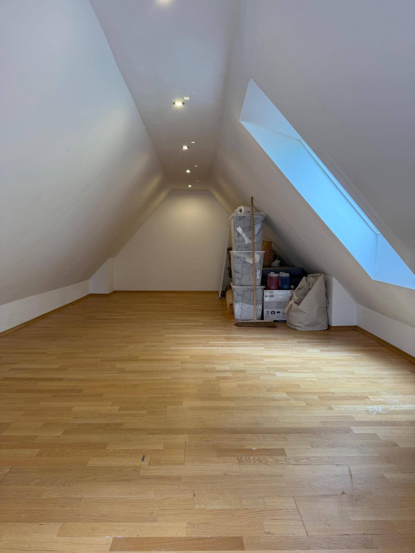 Heller Dachbodenraum mit Holzboden, schrägen Wänden und einem großen Dachfenster.