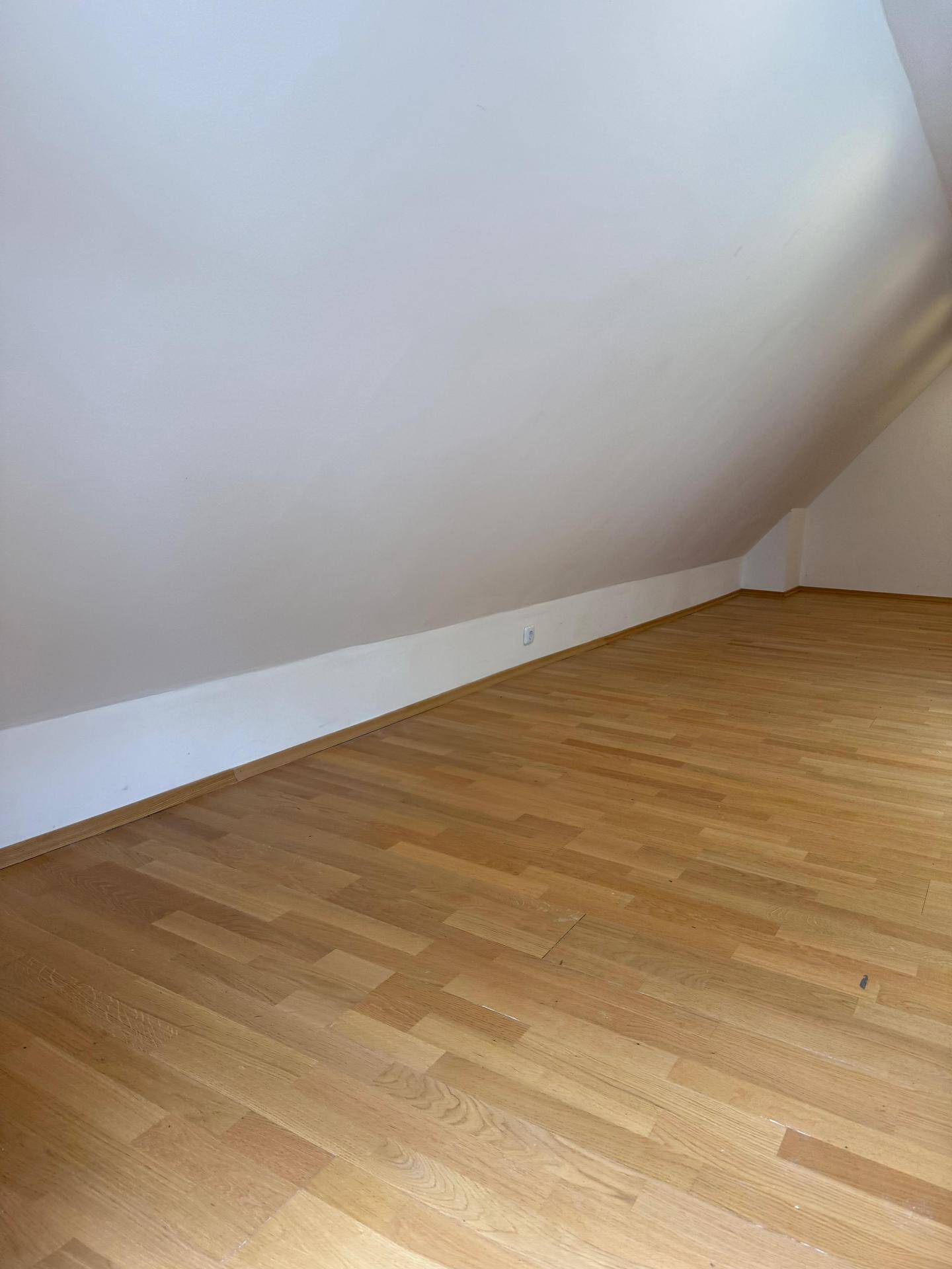 Geräumiger, leerer Dachbodenraum mit hellem Holzboden und schrägen Wänden.