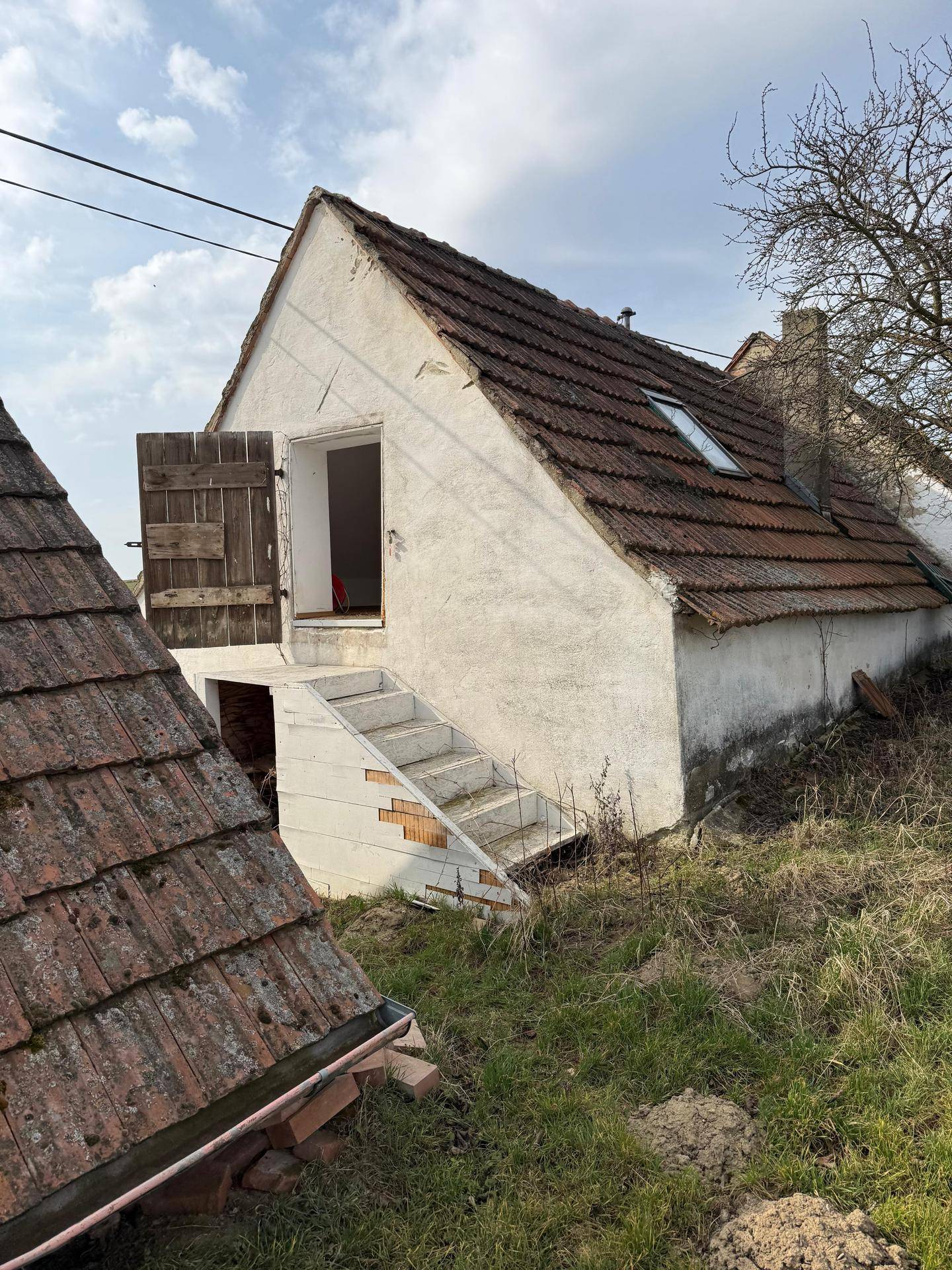 Rückseite eines alten Gebäudes mit Ziegeldach, Außentreppe und Blick auf die Landschaft.