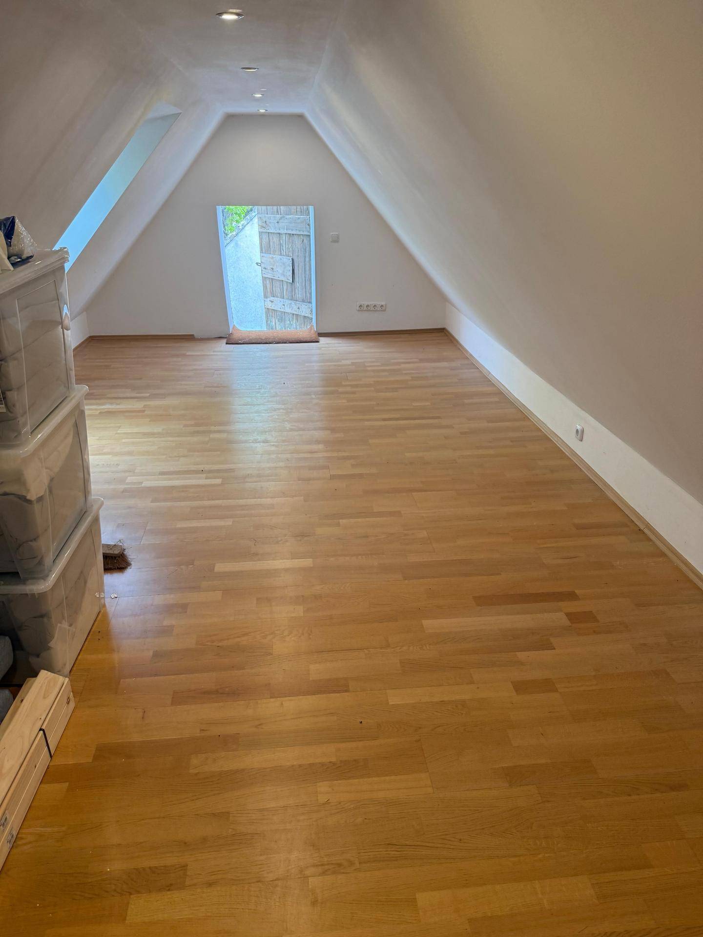 Heller Dachbodenraum mit Holzboden und Blick auf die offene Tür zum Außenbereich.