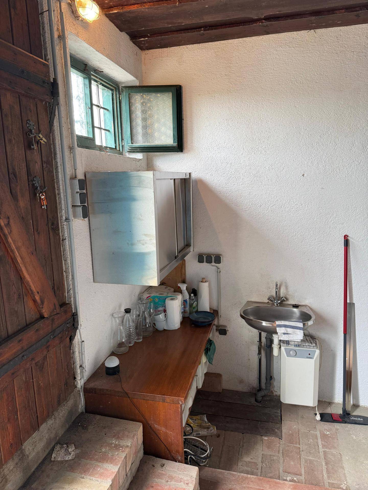 Einfacher Hauswirtschaftsraum mit Spülbecken, Arbeitsplatte und Stauraum unter einem Fenster.