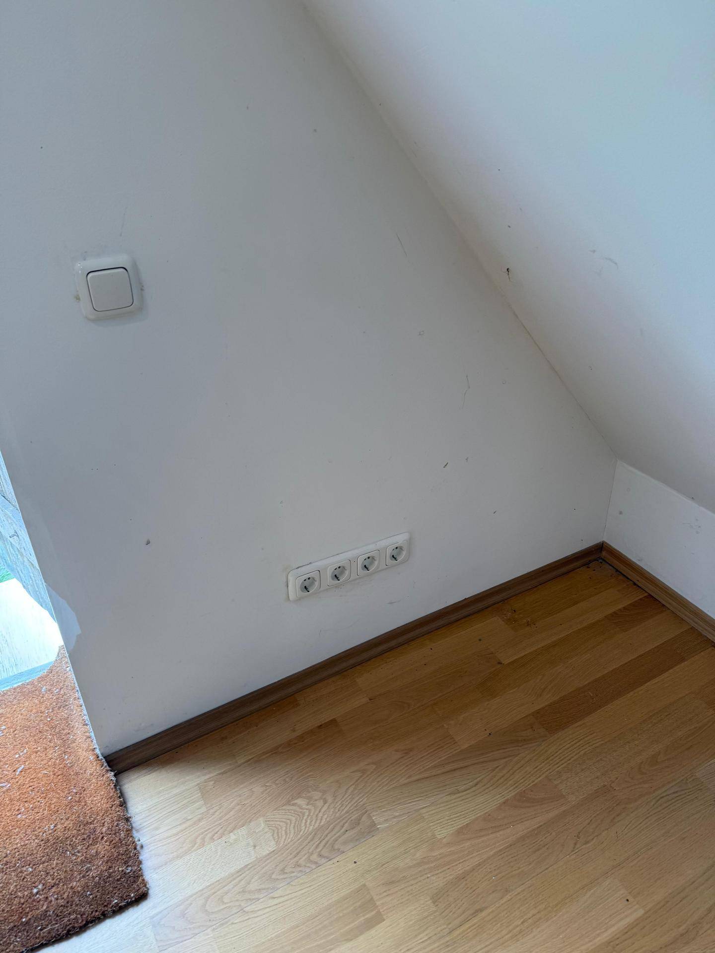 Detailansicht des Dachbodens mit Holzboden und Steckdosen an der schrägen Wand.