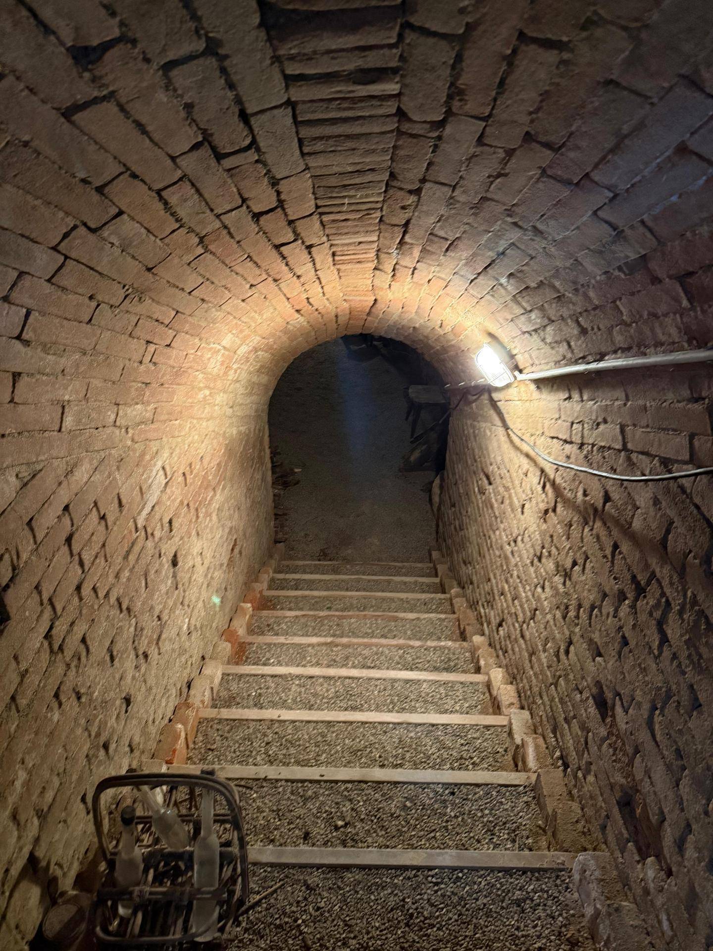 Historischer Gewölbekeller mit Ziegelwänden und Treppe, die in die Tiefe führt.