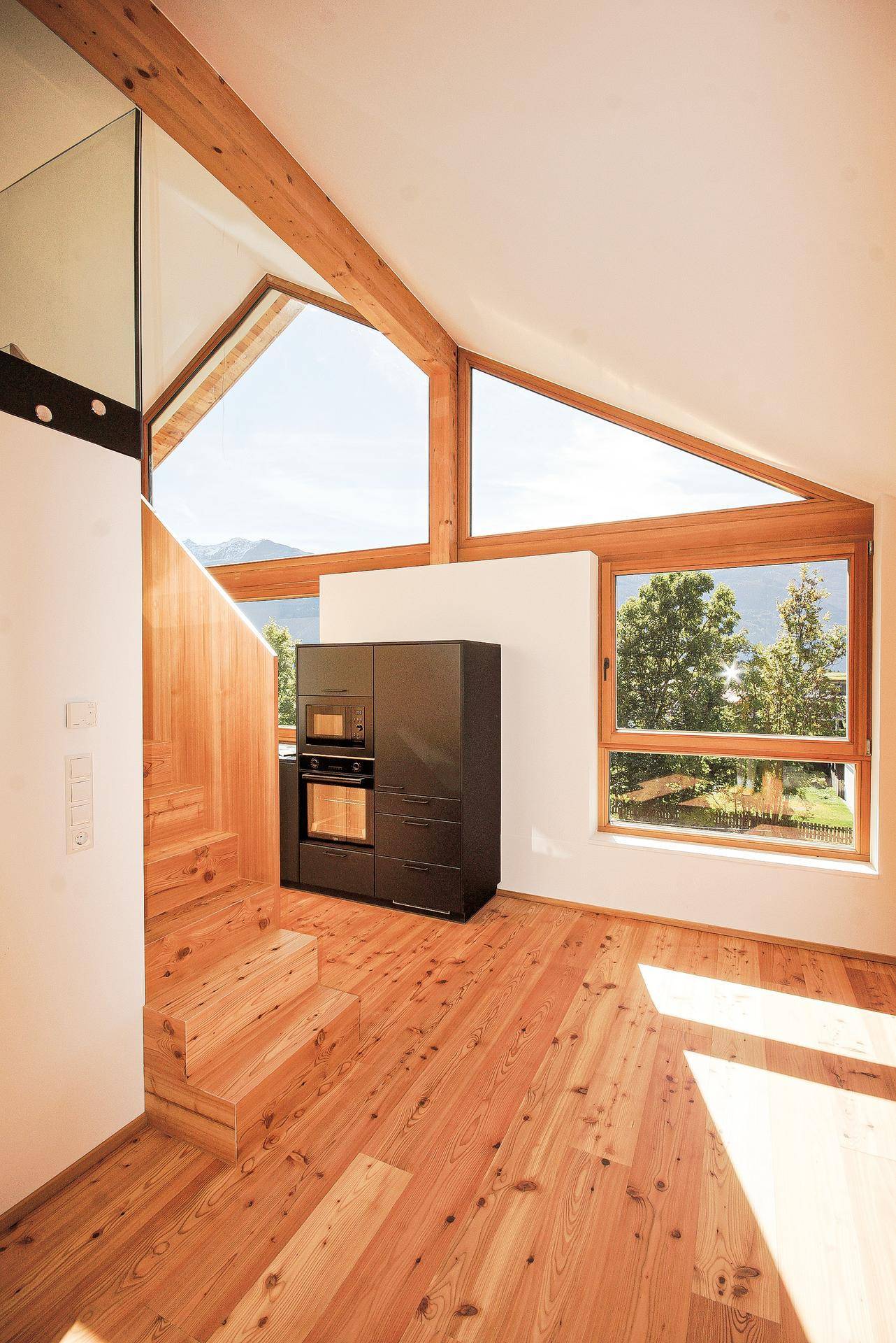 Heller Raum mit Holzboden, sichtbaren Dachbalken, großen Fenstern und integriertem Ofen.