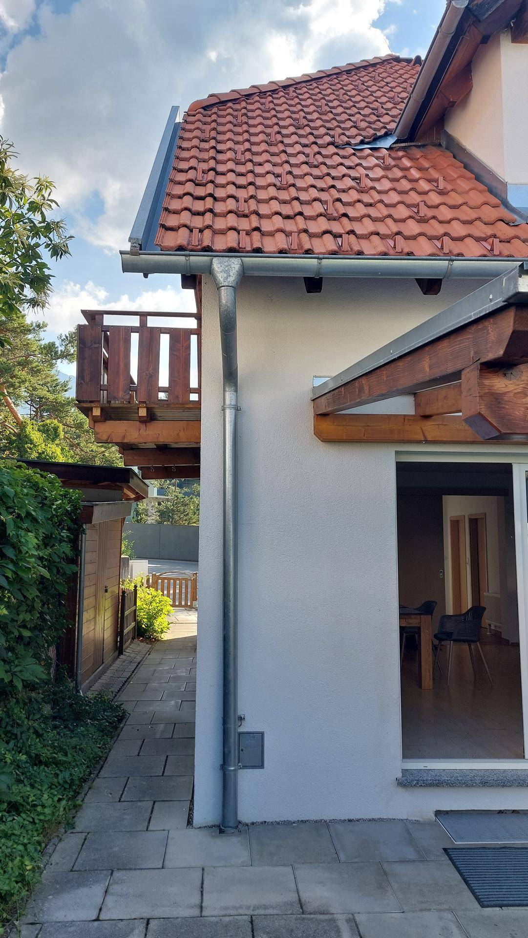 Seitenansicht des Hauses mit Holzbalkon im Obergeschoss und Zugang zum Innenbereich.