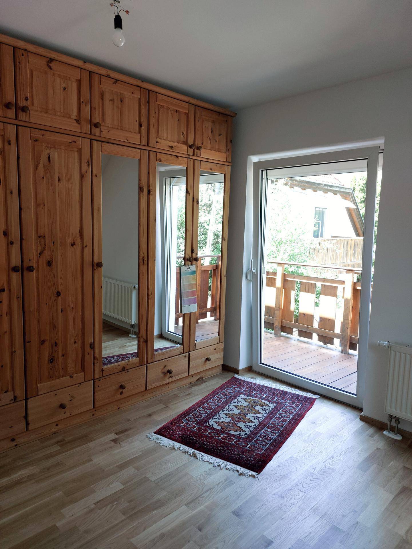 Helles Schlafzimmer mit großem Holzschrank, Holzboden und Zugang zum Balkon.