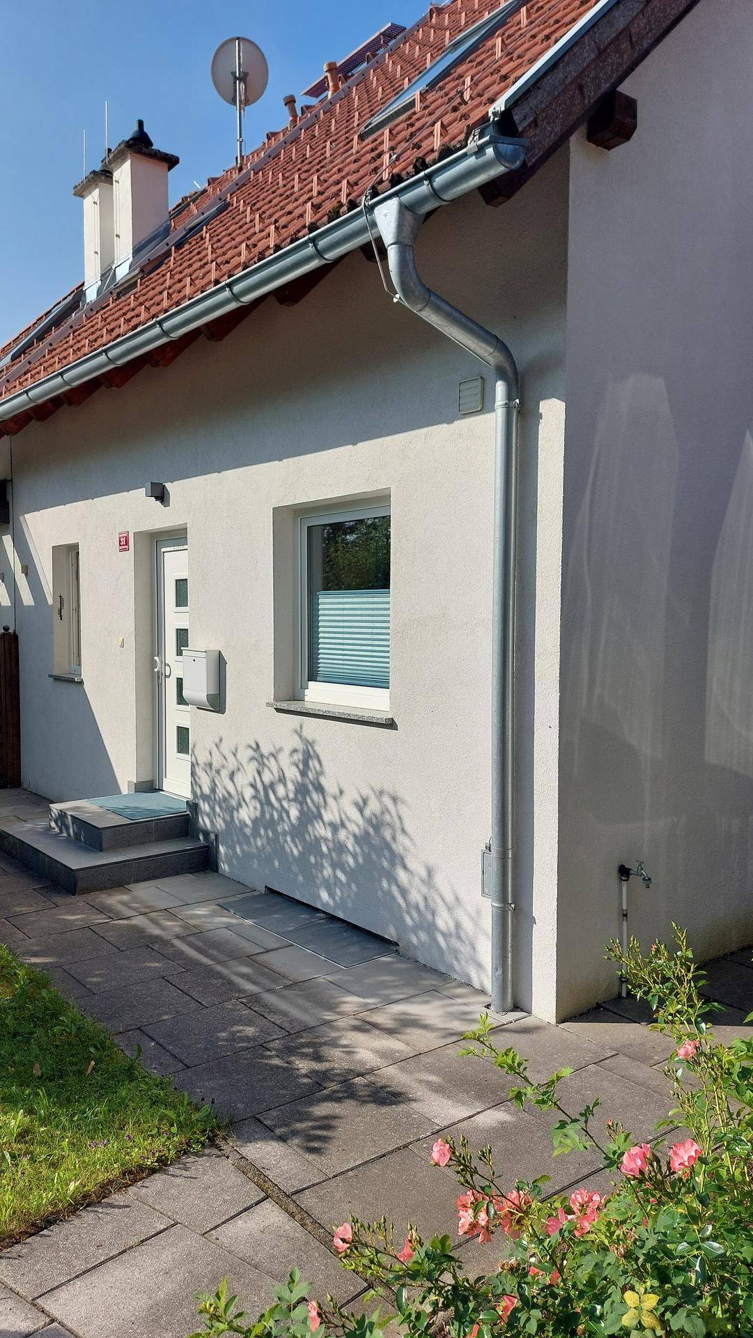 Seitenansicht des Hauses mit weißer Fassade, Eingangsbereich und gepflastertem Weg.