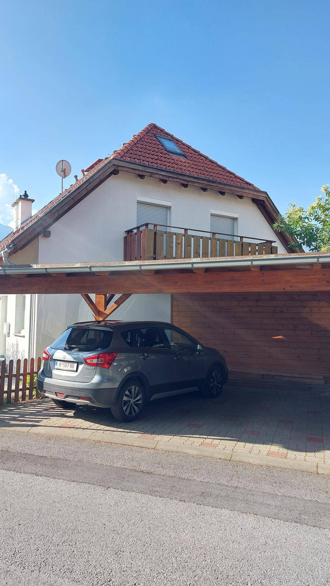 Hausansicht mit Carport und geparktem Auto unter dem roten Ziegeldach.