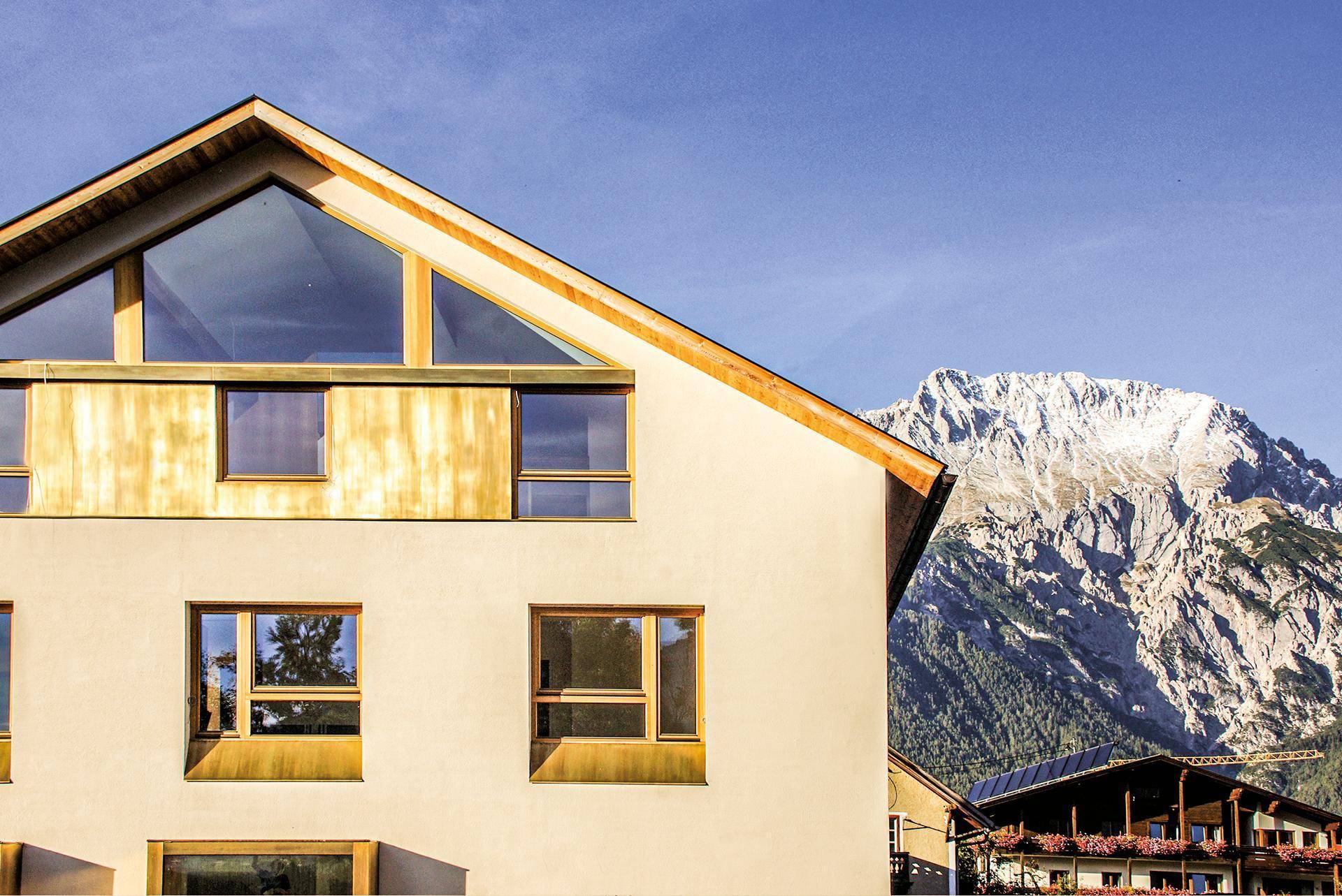 Nahaufnahme der modernen Fassade mit Holzverkleidung, großen Fenstern und beeindruckendem Bergblick.