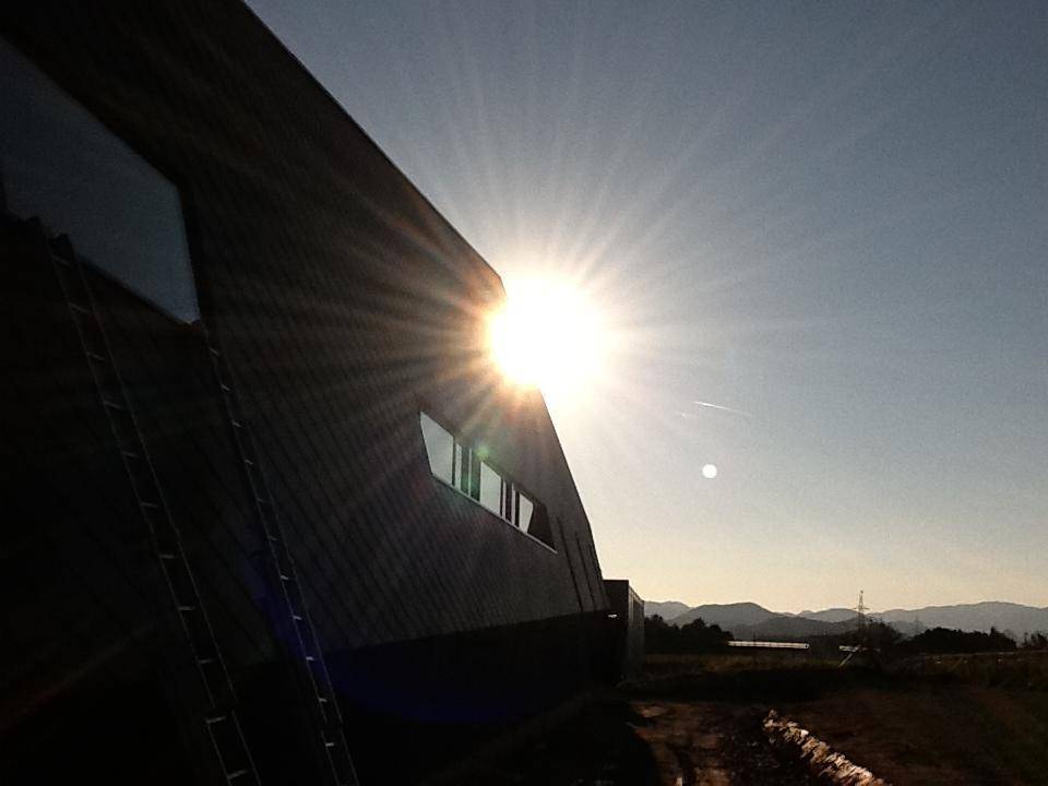 Seitenansicht eines modernen Gebäudes mit schrägen Linien, beleuchtet von der tief stehenden Sonne am Horizont.