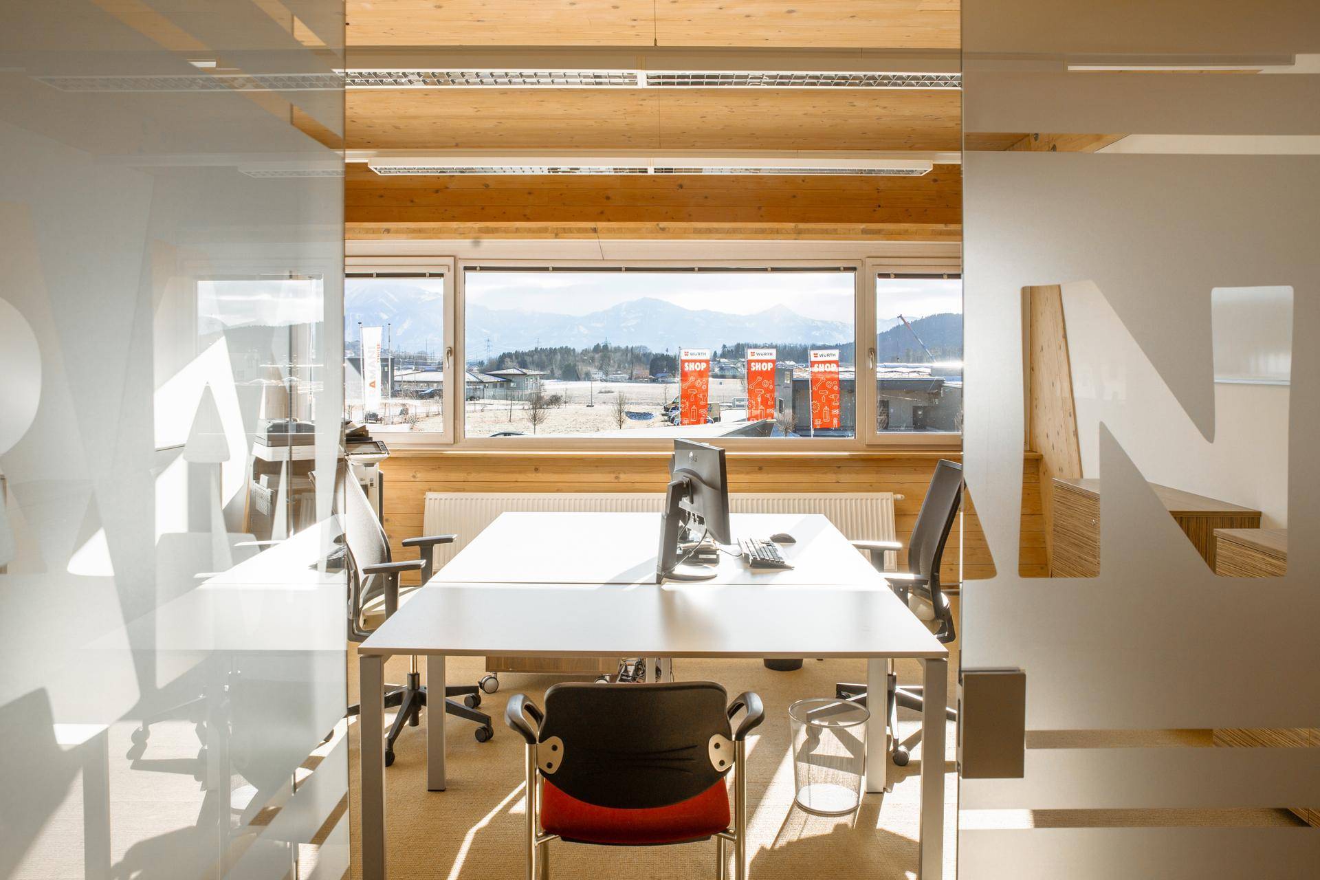 Besprechungsraum mit Glaswänden, Holzwänden und -decke, modernen Tischen und Stühlen sowie Bergblick.