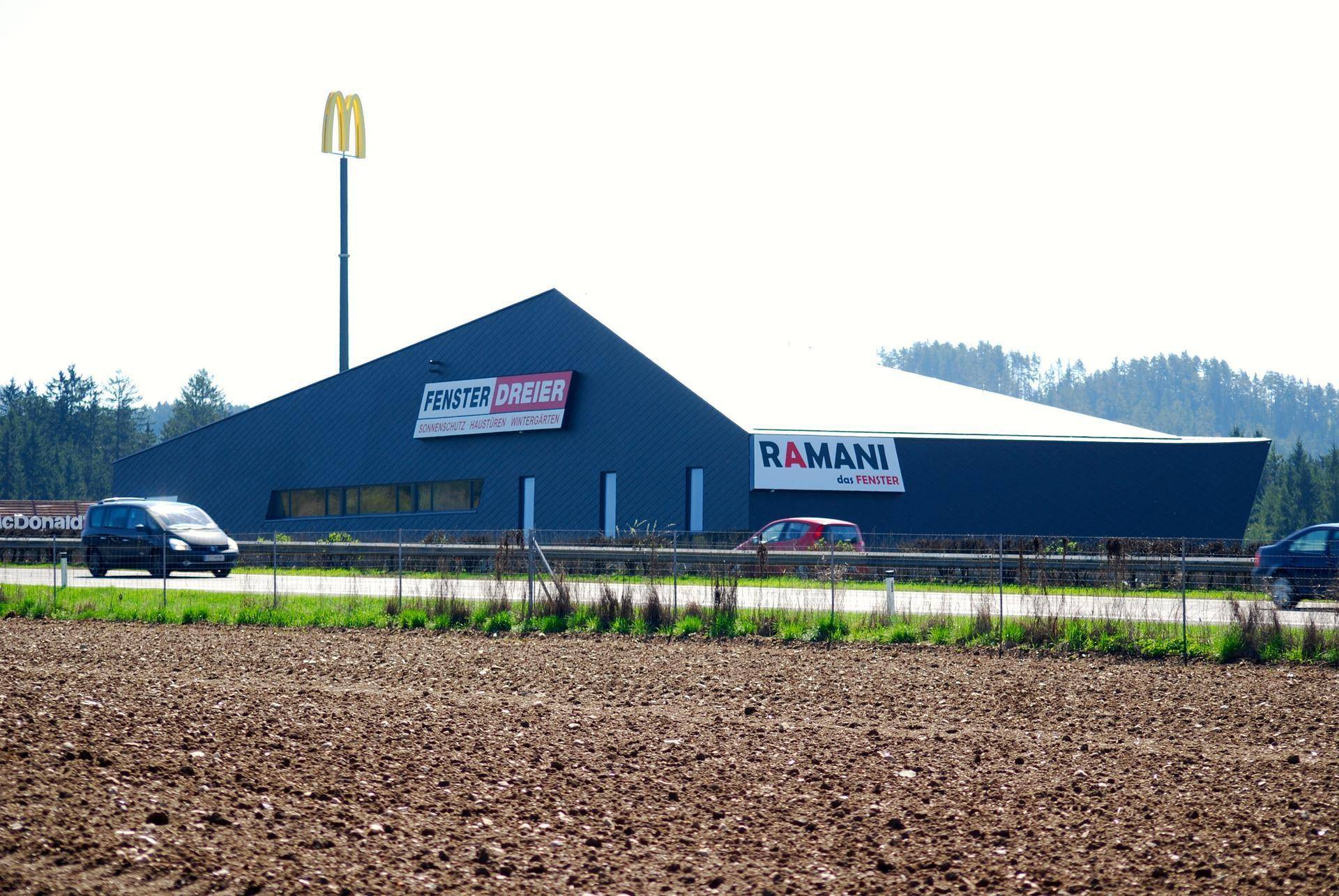 Modernes Geschäftsgebäude an einer Straße mit Firmenlogos und einem McDonald's-Schild im Hintergrund.