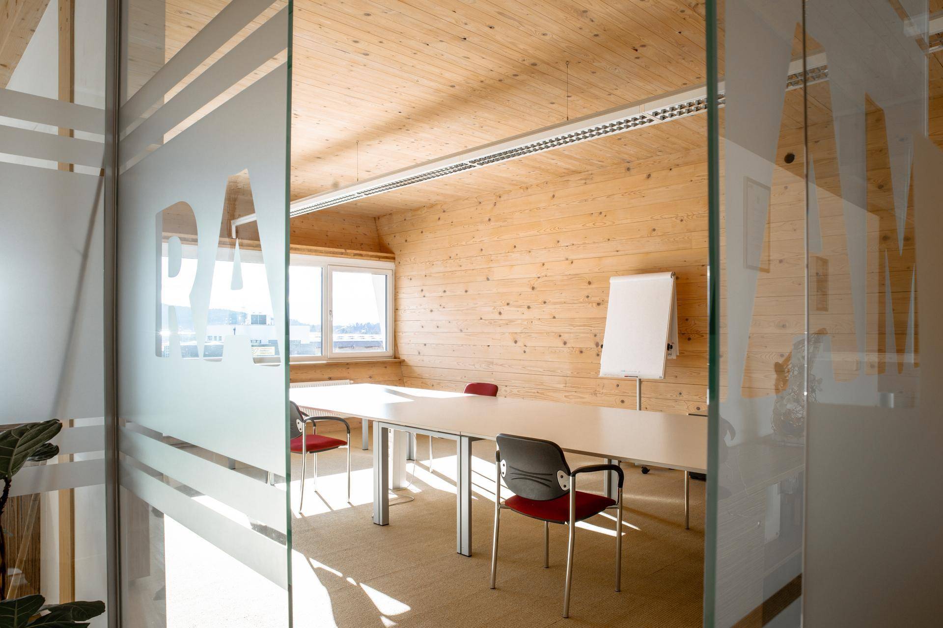 Heller Besprechungsraum mit Holzwänden und -decke, modernen Möbeln und einem Whiteboard für Präsentationen.