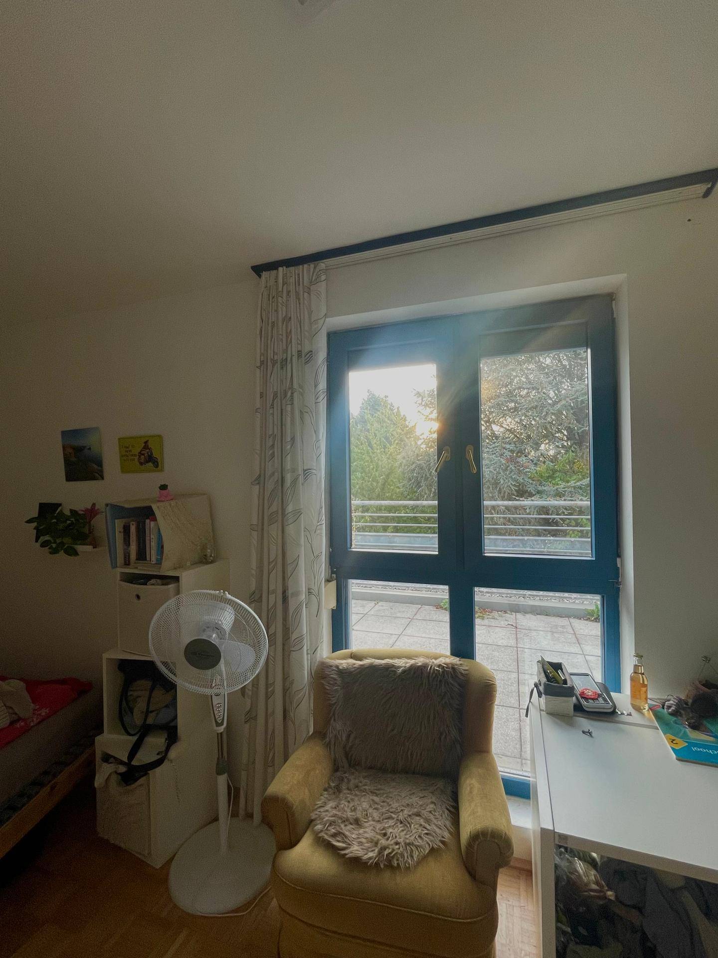 Sonnenlicht durchflutet das Zimmer durch die große Balkontür, mit Blick ins Grüne.