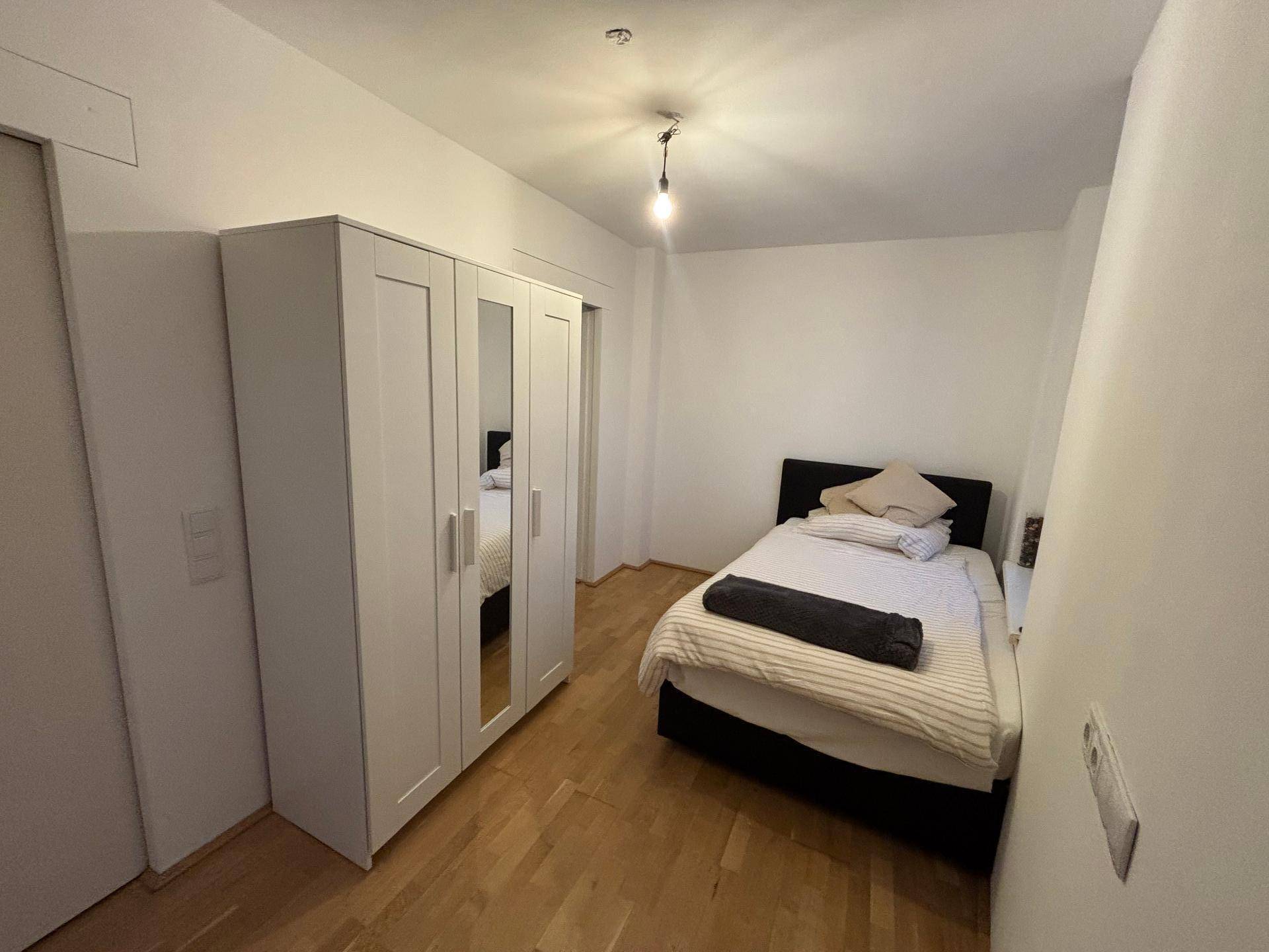 Gemütliches Schlafzimmer mit Holzboden, einem Einzelbett und einem weißen Kleiderschrank mit Spiegeltüren.