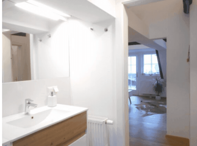 Helles Badezimmer mit Waschbecken und Spiegel, mit Blick in den angrenzenden Wohnbereich.
