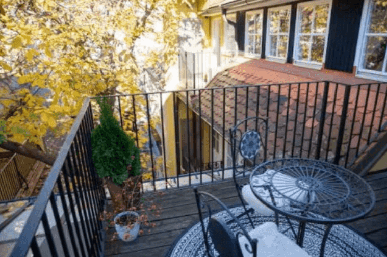 Kleiner Balkon mit schmiedeeisernen Möbeln und Blick auf herbstliche Bäume und Dächer.