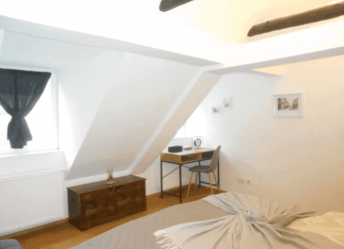 Helles Schlafzimmer mit Schreibtisch, Kommode und charakteristischer Dachschräge.