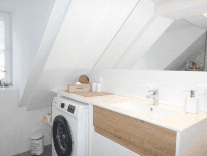 Modernes Badezimmer mit Waschbecken, großem Spiegel und integrierter Waschmaschine unter der Dachschräge.