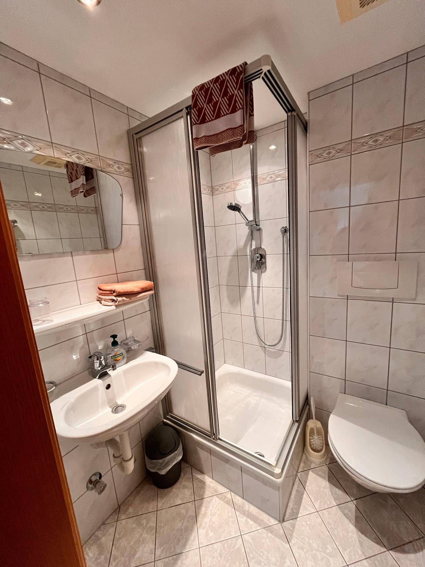 Funktionales Badezimmer mit Duschkabine, Waschbecken und WC, komplett gefliest.